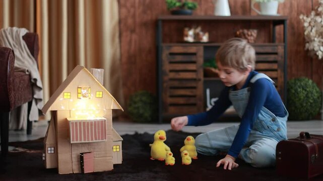 Child, cute boy, playing with toys in a playroom, teddy bear and little ducks with a paper house