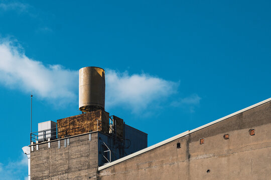 This image features a vintage water tower atop an industrial building, contrasted beautifully by a vibrant blue sky and fluffy white clouds, radiating character and nostalgia.