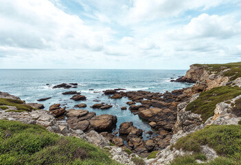 A rocky shoreline with a body of water in the background. The water is calm and the rocks are scattered throughout the area. The scene is peaceful and serene, with the ocean