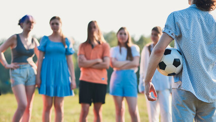 Obraz premium Young man is holding a soccer ball and facing a group of friends in a field on a sunny day.