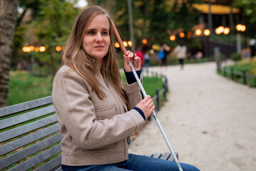 A visually impaired woman with white cane sitting at park