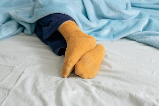Child sleeping peacefully in bed wearing yellow socks and covered by blue blanket