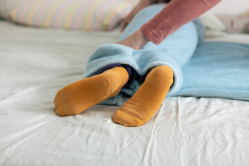 Mother tucking child into bed with blue blanket and yellow socks