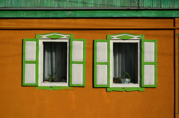 Obraz premium two windows with shutters on the orange wall of the house