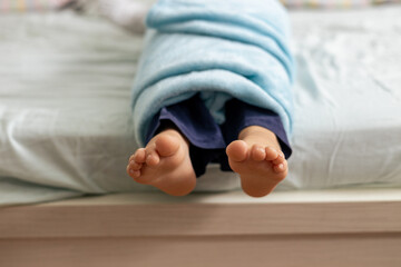 Child feet covered with blue blanket lying on bed