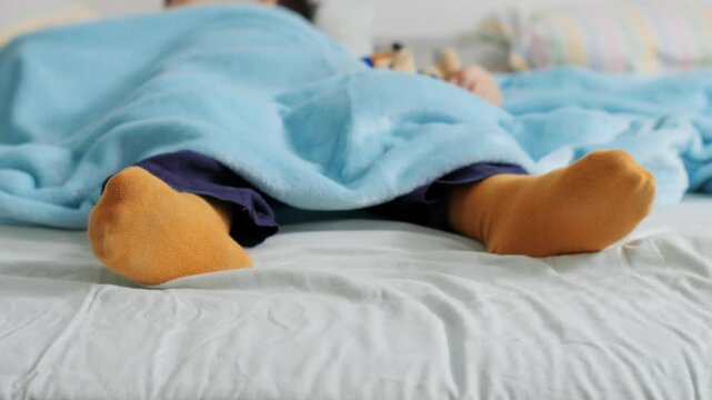 Child sleeping peacefully in bed wearing yellow socks and covered by blue blanket