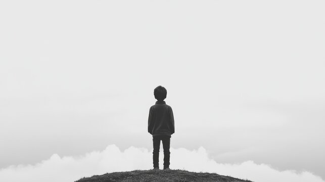 Solitary child standing on hilltop, gazing at cloudy sky.