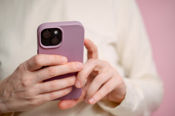 Close up of female hand using smartphone isolated on pink wall.