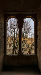 View of the medieval architecture of Carcassonne through a window with two stone arches on a cloudy day.