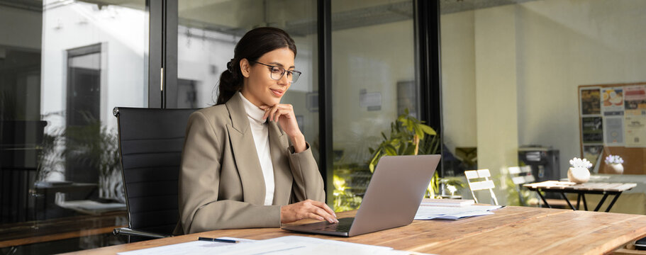Young businesswoman professional employee using pc doing online banking analysing at workplace. Latin hispanic middle age business woman working on laptop computer in modern office. Banner, copy space