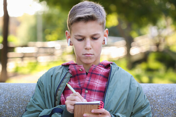 Teenager writing in the notebook sitting on a bench outdoors