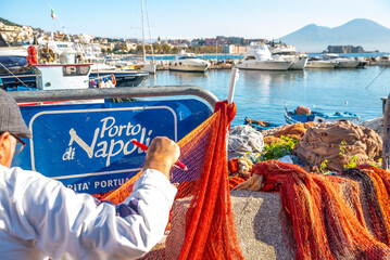 Boat dock in Naples. An old fisherman weaves a fishing net. A sign in Italian that says 