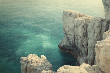 Serene coastal scene featuring rugged, light-colored cliffs and a tranquil teal sea.