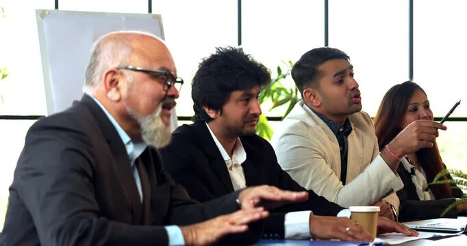 Indian Asian group of four successful business professionals in executive attire, sitting at one side of the conference table, discussing or interviewing someone