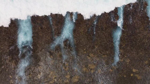 Drone top down texture of ocean waves crashing and draining over shallow fringing reef