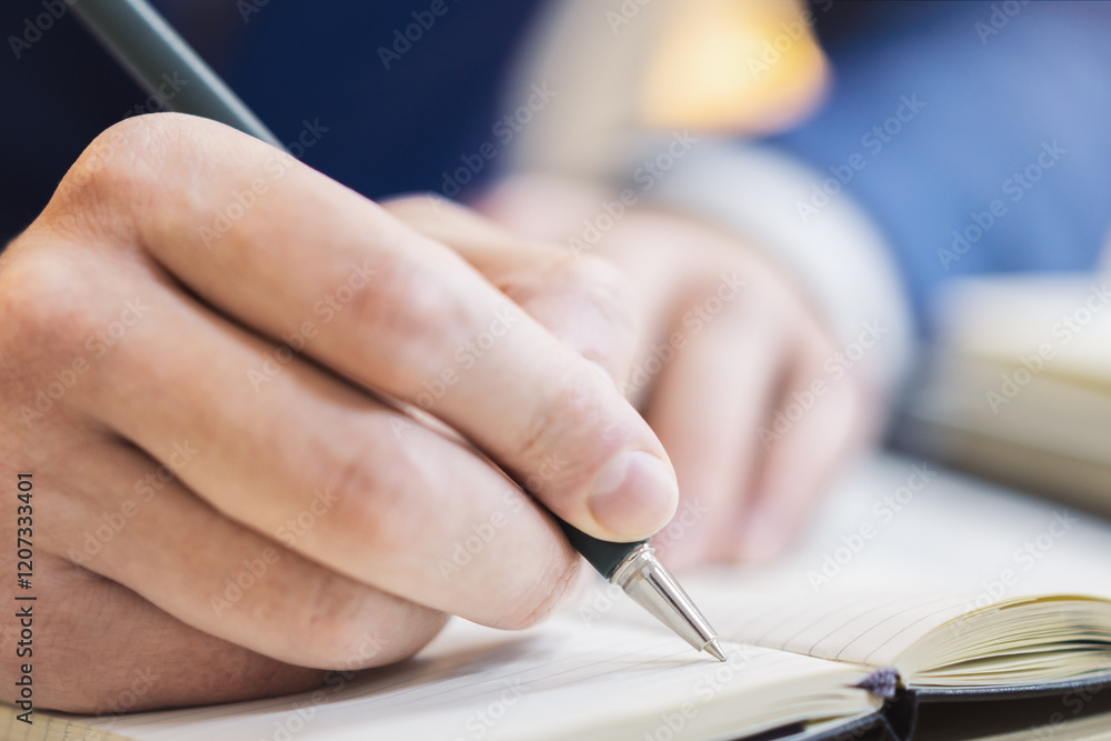 Poster Close-up capture of a man's hand as he writes in a notepad, with an out-of-focus background