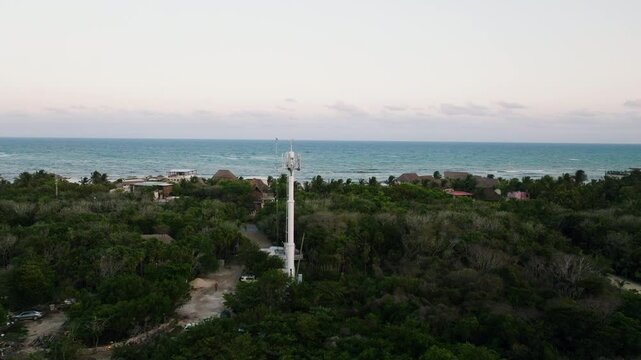 Drone revealing La Veleta beachside eco resort cottages surrounded by Caribbean coast and tropical forest landscape in evening, Tulum town neighbourhood