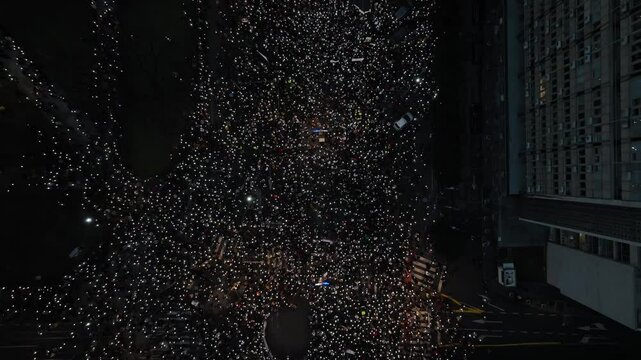 Protest in the streets with thousands of people raising their phones in the air to illuminate the night