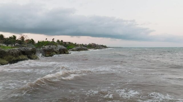 Strong ocean tides crashing into rocks from Caribbean sea with Azulik eco resort landscape near shoreline, Tulum, Quintana Roo, Tracking drone shot