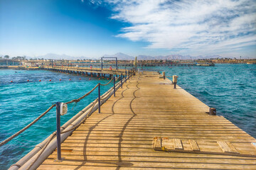 A sun-drenched wooden pier extends into a vibrant turquoise sea. Gentle waves lap against the structure, offering a tranquil scene of coastal serenity. 