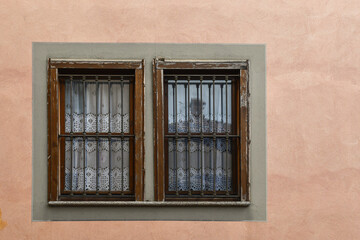 Detail of the facade of an old house with a pair of windows with lace curtains, Piedmont, Italy