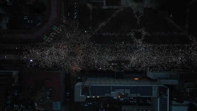 Aerial footage of a large crowd illuminating the night with their phones during the protests.