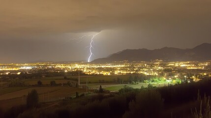 Night cityscape with lightning strike over mountains.