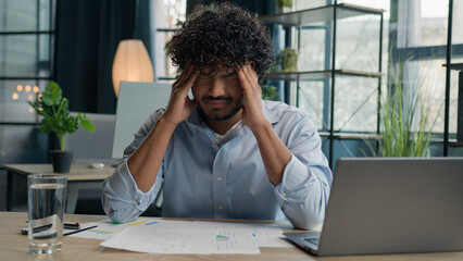Sick exhausted Arabian Indian latino man guy working on laptop business paperwork overworked male...