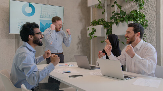 Happy team colleagues celebrate winning business deal achieve victory give high five multiethnic businessmen and muslim businesswoman in hijab working in boardroom office unity partnership teamwork