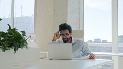 Anxious depressed Indian Arabian man stressed businessman working laptop in office distant job male...
