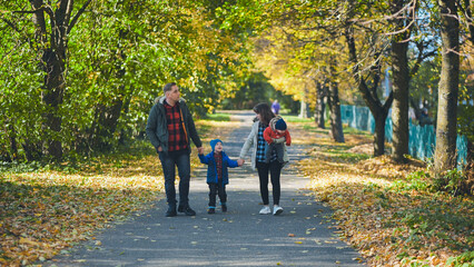 Fototapeta premium Family walking together on autumn path, sharing laughter among golden fallen leaves under warm sunlight