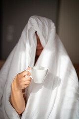 Woman with cup of coffee in the morning under the blanket at home