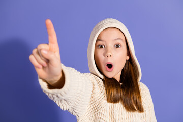 Surprised young girl with a hoodie pointing in the air against a purple background
