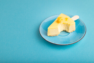 bitten Yellow Cake pop with sprinkles on blue ceramic plate on blue pastel paper, side view, copy space