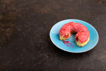 bitten Pink Donut with sprinkles on blue ceramic plate on black concrete, side view, copy space