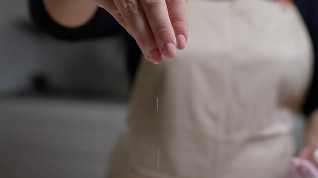 Hand sprinkling salt close up, adding seasoning for cooking in a kitchen.