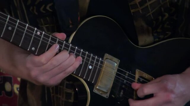 Closeup left handed guitarist bends strings on black electric guitar