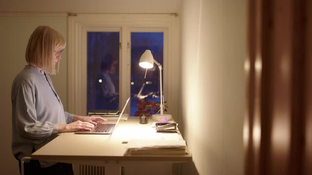 Female entrepreneur use standing desk to work online on laptop at night