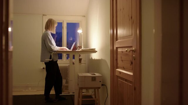 Woman hustling online on laptop at night use standing desk for improved posture