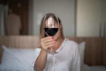 Young beautiful woman with a glass of wine sitting on the bed.