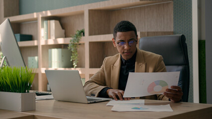 African American man entrepreneur office manager guy male businessman working at desk with laptop read documents check graphics charts business paperwork analyzing data upset financial problem mistake