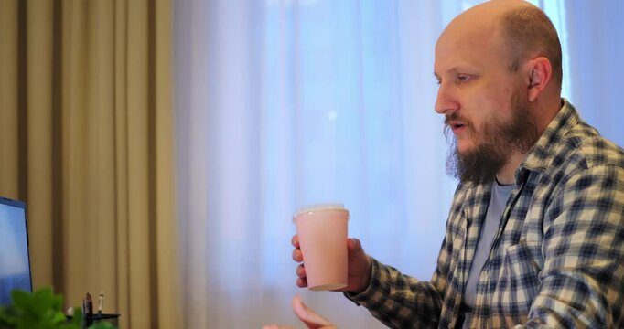 Bald man talking on video call, revealing fatigue from nonstop work, letting fatigue erode mental clarity, cautioning how fatigue undermines well-being without proper breaks. Drinks coffee