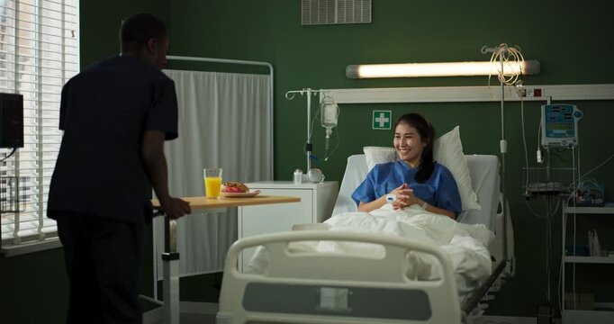 Young woman recovers in a hospital room. An African doctor delivers her breakfast.