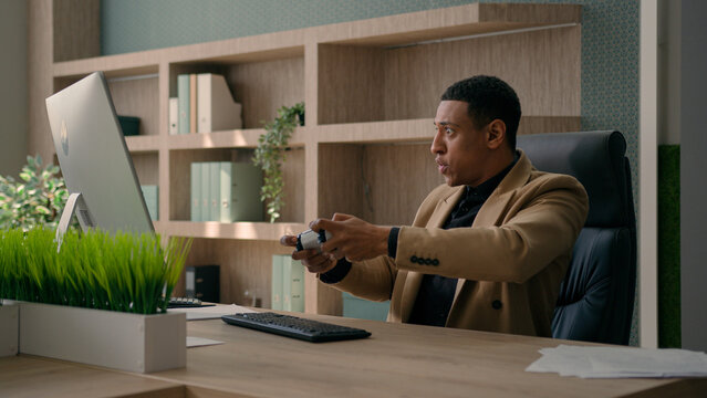 Funny African American office worker employee businessman playing online video game on computer take break fun entertainment humor male lazy business man fooling hide joystick pretend working smiling