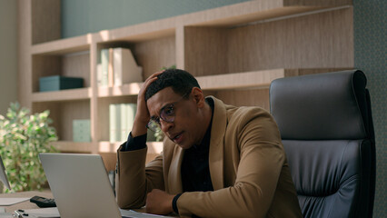 African American stressed businessman working laptop business documents paperwork problem financial...