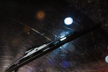 dirty and blurry windshield with windshield wiper, at night time against the background of a blurred image of a traffic light and street lighting, danger of poor visibility on the road