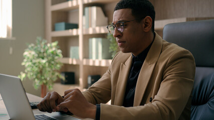 Fototapeta premium Focused African American man businessman working with corporate documents sales research professional employer office manager business CEO chief typing data on laptop computer analytics commerce work