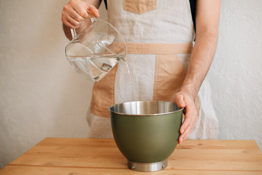 male baker pours water into a bowl of flour