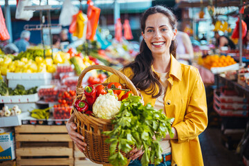 Smiling Woman Holding a Basket of Fresh Vegetables at a Vibrant Market