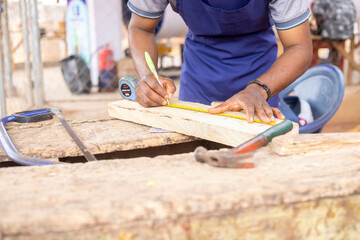 Carpenter measuring a piece of wood with a ruler and pencil on a workbench featuring tools such as...